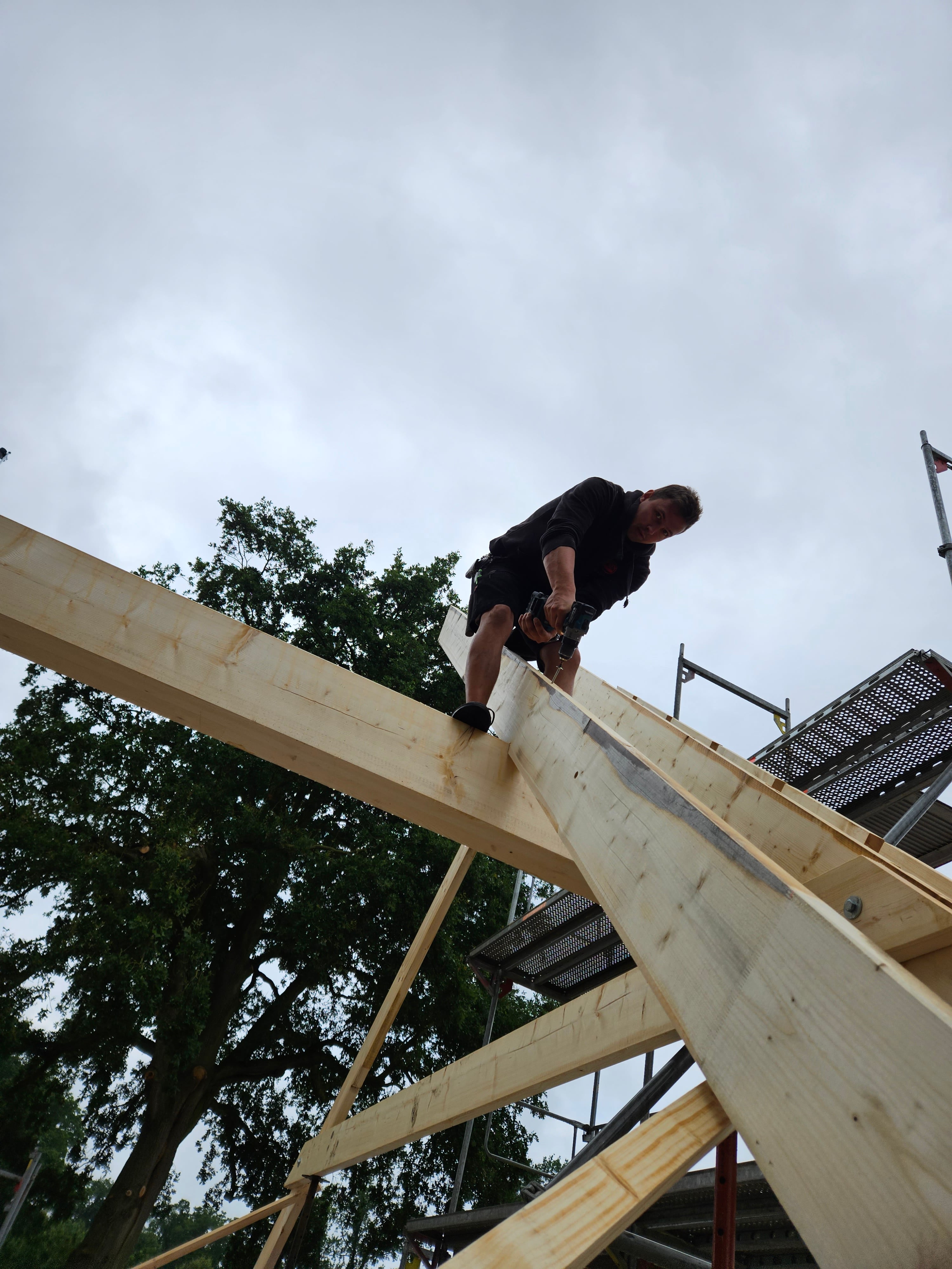 Ein Mann auf einem Dachstuhl mit einer Bohrmaschine.